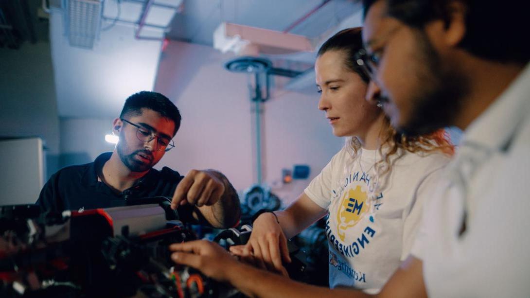 Three Kettering mechanical engineering students inspect car parts in the Car Lab